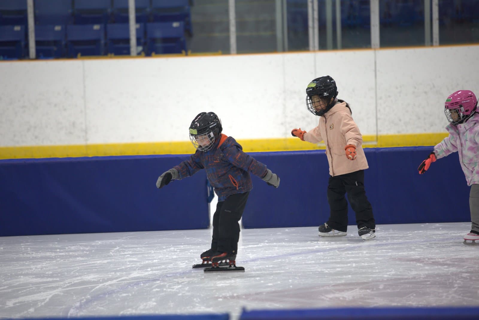 Three young Learn to Skate kids in helmets practicing on the ice.
